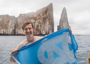 Jackson Seymore holds up a UNC flag while out on the water, a large rock face behind him. 