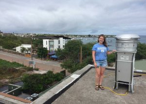 Tessa Szalkowski stands on a rooftop in Galapagos next to some large metal equipment. 
