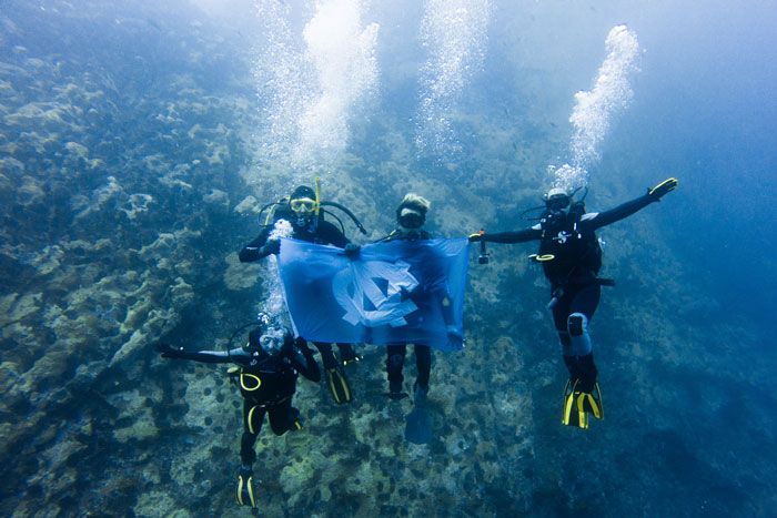 Four people in scuba diving equipment underwater, holding up a UNC-Chapel Hill flag