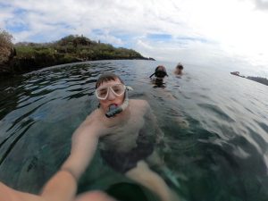 Wide lens selfie of Jonathan Collins in the water wearing goggles and a snorkel, two other snorkelers behind him.