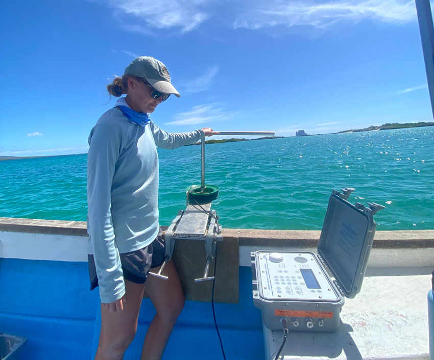 Savannah Ryburn operating a hydrophone (metal rod-like piece of equipment attached to a large computer-type piece of technology) on a boat.