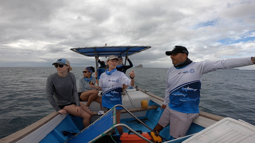 Savannah Ryburn gesturing while in a boat with 5 other researchers.