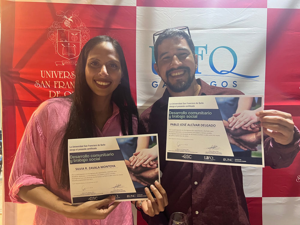 Siliva Zavala (left) and Pablo Alcívar hold up certificates from the program in front of a USFQ-branded banner.